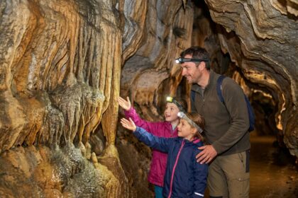 Famille explorant une grotte à stalactites en Dordogne, père et deux enfants avec lampes frontales