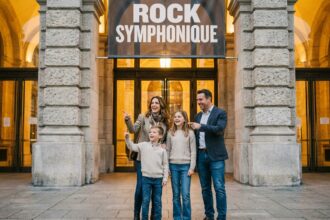 Famille de quatre personnes devant une salle de concert symphonique avant un concert de rock, souriante et enthousiaste