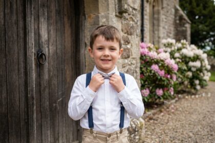 Jeune garçon souriant ajustant sa cravate devant une porte en bois